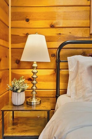 A wooden wall with a metal bed frame and a bedside table with a lamp and a small potted plant. - Renovated Log Cabin | Mins to Heavenly & Beach (South Lake Tahoe)