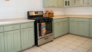 A kitchen with light green cabinets, a stainless steel stove, and a tiled floor.