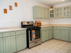A kitchen with light green cabinets, a stainless steel stove, and a tiled floor.