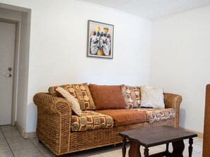 Un salon avec un canapé en osier, une table basse et une œuvre d’art encadrée accrochée au mur.
