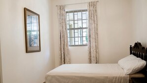 A bedroom with a bed, a window with curtains, a headboard, and a wall-mounted picture frame.