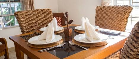 A dining table set with white napkins, plates, cutlery, and woven placemats.