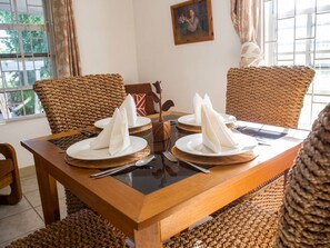 Une table à manger dressée avec des serviettes blanches, des assiettes, des couverts et des sets de table en fibres tressées.