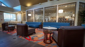 Un espace de détente moderne, avec des canapés, des fauteuils et une table basse, agrémenté de murs à motifs et d’une grande fenêtre.
