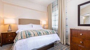 Una habitación de hotel con cama, dos mesitas de noche, cómoda, espejo y ventana con cortinas.