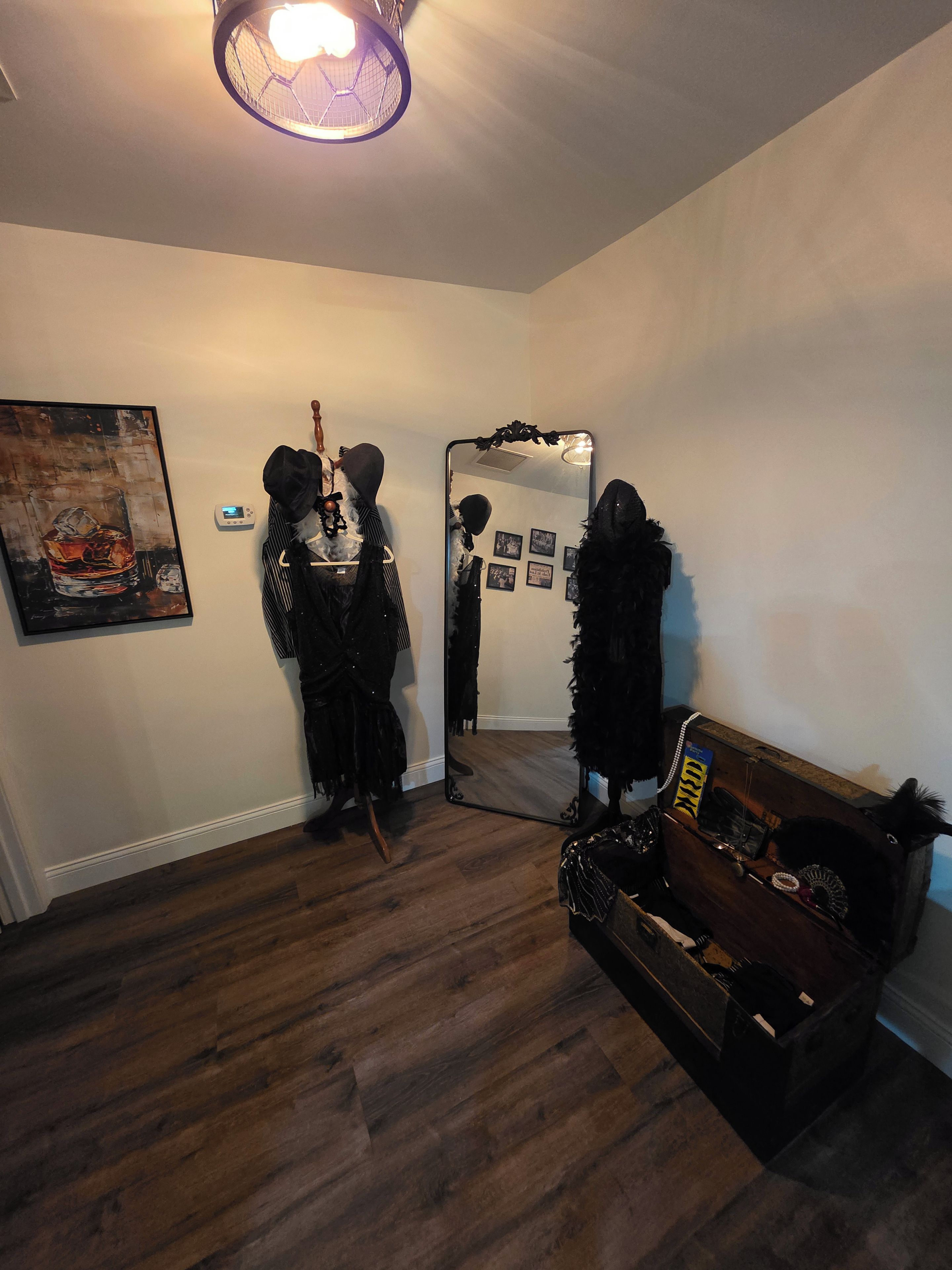 A room with a wooden floor, a mirror, a coat rack, and a painting.