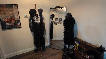 A room with a wooden floor, a mirror, a coat rack, and a painting.