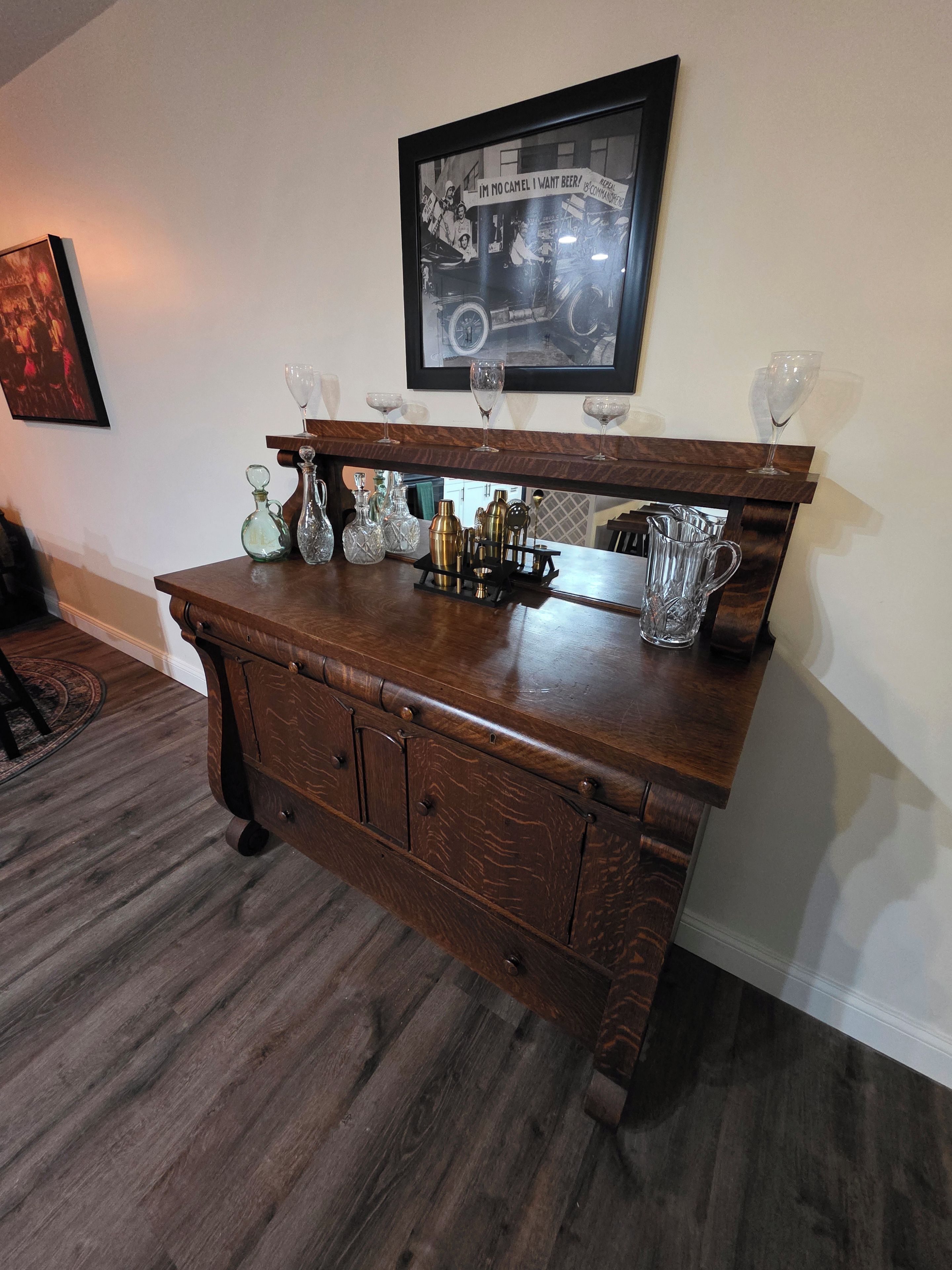 A wooden bar with a vintage car photo, wine glasses, and barware.
