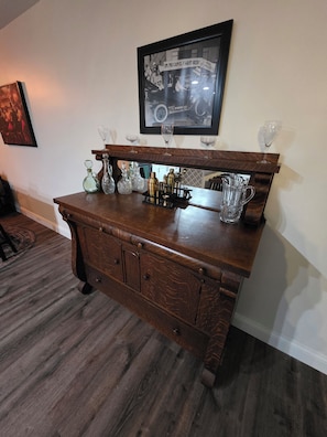A wooden bar with a vintage car photo, wine glasses, and barware.