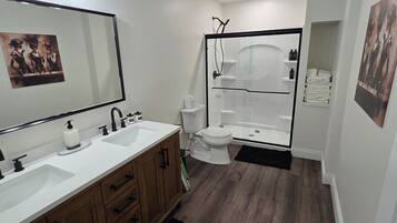 A modern bathroom with a double sink vanity, a glass shower enclosure, and a toilet.