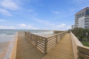 A wooden boardwalk leading to a beach with a clear view of the ocean and a multi-story building in the background. - Luxury Oceanfront Escape at “Top of the Regis” (North Topsail Beach)