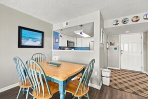 A dining area with a wooden table and chairs, a kitchen with white cabinets and a microwave, and a hallway with a patterned rug. - Luxury Oceanfront Escape at “Top of the Regis” (North Topsail Beach)