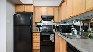 Cozinha compacta com geladeira preta, forno embutido, micro-ondas e armários de madeira.