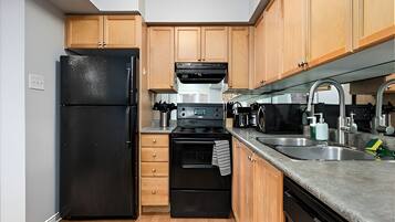 A compact kitchen with a black refrigerator, a built-in oven, a microwave, and wooden cabinets.