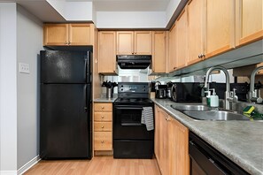 A compact kitchen with a black refrigerator, a built-in oven, a microwave, and wooden cabinets. - Comfort Townhouse Suites (Mississauga)