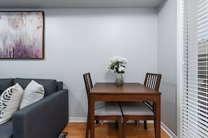 Un coin repas avec une table et des chaises en bois, un vase rempli de fleurs blanches et un canapé gris agrémenté de coussins à motifs.