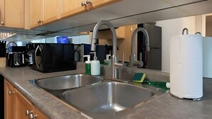 Cozinha com duas pias de aço inoxidável, armários de madeira, cafeteira e eletrodoméstico branco.