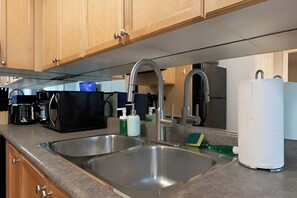 A kitchen with two stainless steel sinks, wooden cabinets, a coffee maker, and a white appliance. - Comfort Townhouse Suites (Mississauga)