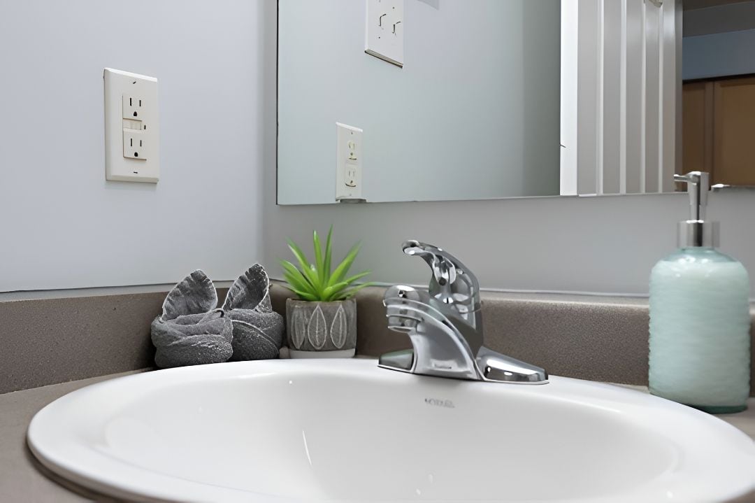 Un baño con un lavamanos blanco, un espejo, un perchero para toallas y una pequeña planta en maceta.