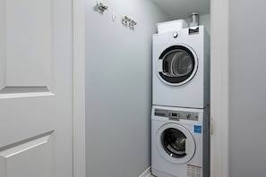 A compact laundry room with a stacked washer and dryer, a white door, and a wall-mounted towel dispenser. - Comfort Townhouse Suites (Mississauga)