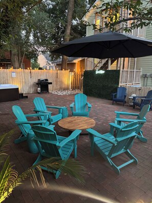 Eine Außenpatio mit einem Holztisch, umgeben von Türkis-farbenen Adirondack-Stühlen, einem Grill und einem Whirlpool.