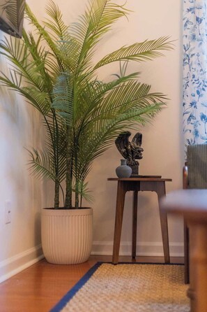 Canto de um quarto com uma planta em vaso, uma mesa pequena com uma estátua e uma cadeira.