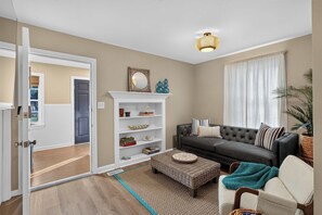 A living room with a sofa, a coffee table, a bookshelf, and a door leading to another room. - Savannah Reserve Whole House & Hot Tub Sleeps 12 (Savannah)