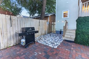 A backyard with a barbecue grill, a wooden fence, and a paved patio area. - Savannah Reserve Whole House & Hot Tub Sleeps 12 (Savannah)
