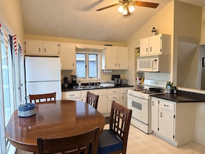 A kitchen with white cabinets, a stove, a sink, and a dining table with chairs. - Beautiful Gun Lake Cottage – Private Lakefront, Sandy Bottom & Lots of Lake Toys (Middleville)