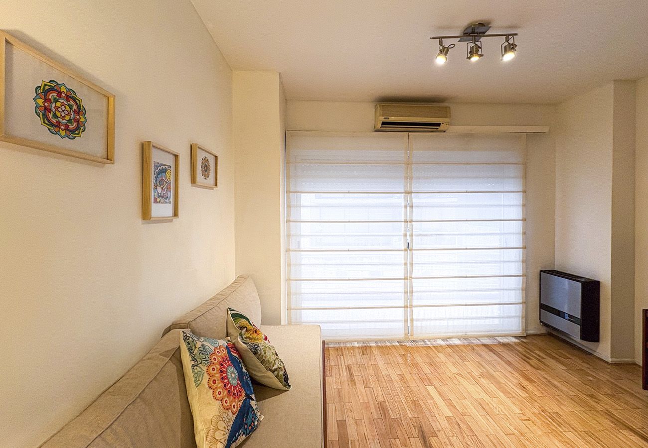 A living room with a sofa, a television, and a large window with blinds.