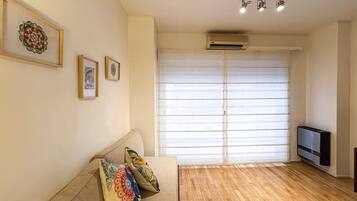 A living room with a sofa, a television, and a large window with blinds.