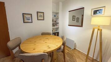 Ein Zimmer mit einem runden Holztisch, vier Stühlen, einem Bücherregal, einem Spiegel und einer Stehlampe.