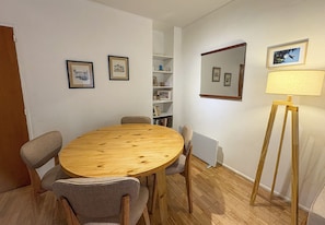Ein Zimmer mit einem runden Holztisch, vier Stühlen, einem Bücherregal, einem Spiegel und einer Stehlampe.