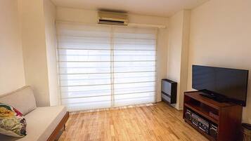 A living room with a sofa, a television on a wooden stand, and a window with blinds.