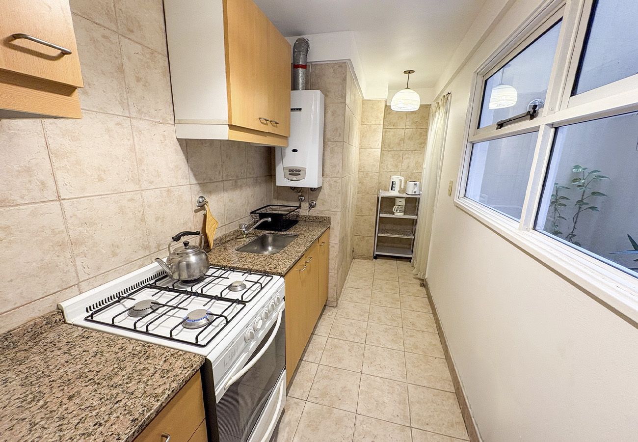 A kitchen with a gas stove, oven, and a sink. There is a window with a view of the outside.