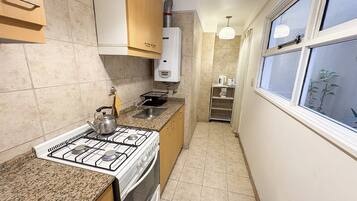A kitchen with a gas stove, oven, and a sink. There is a window with a view of the outside.