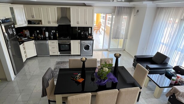 A modern kitchen with white cabinets, a dining table with chairs, and a view to the outside. - Spacious 2-story penthouse with 2 terraces, views of the sea and mountains. (Mahmutlar)