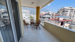 A balcony with a table and chairs, a view of the cityscape, and a building with a sign. - Spacious 2-story penthouse with 2 terraces, views of the sea and mountains. (Mahmutlar)