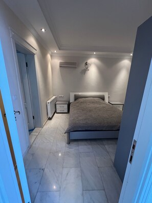 Ein Schlafzimmer mit einem Bett, Nachttischen, einer Klimaanlage und einer Tür zu einem anderen Raum.