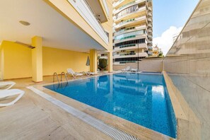 Ein Schwimmbecken mit Liegestühlen und einem Gebäude im Hintergrund.