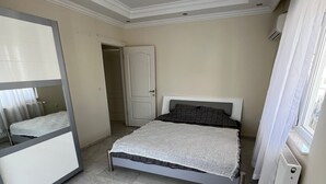 A bedroom with a bed, a mirror, a radiator, and a door. - Spacious 2-story penthouse with 2 terraces, views of the sea and mountains. (Mahmutlar)