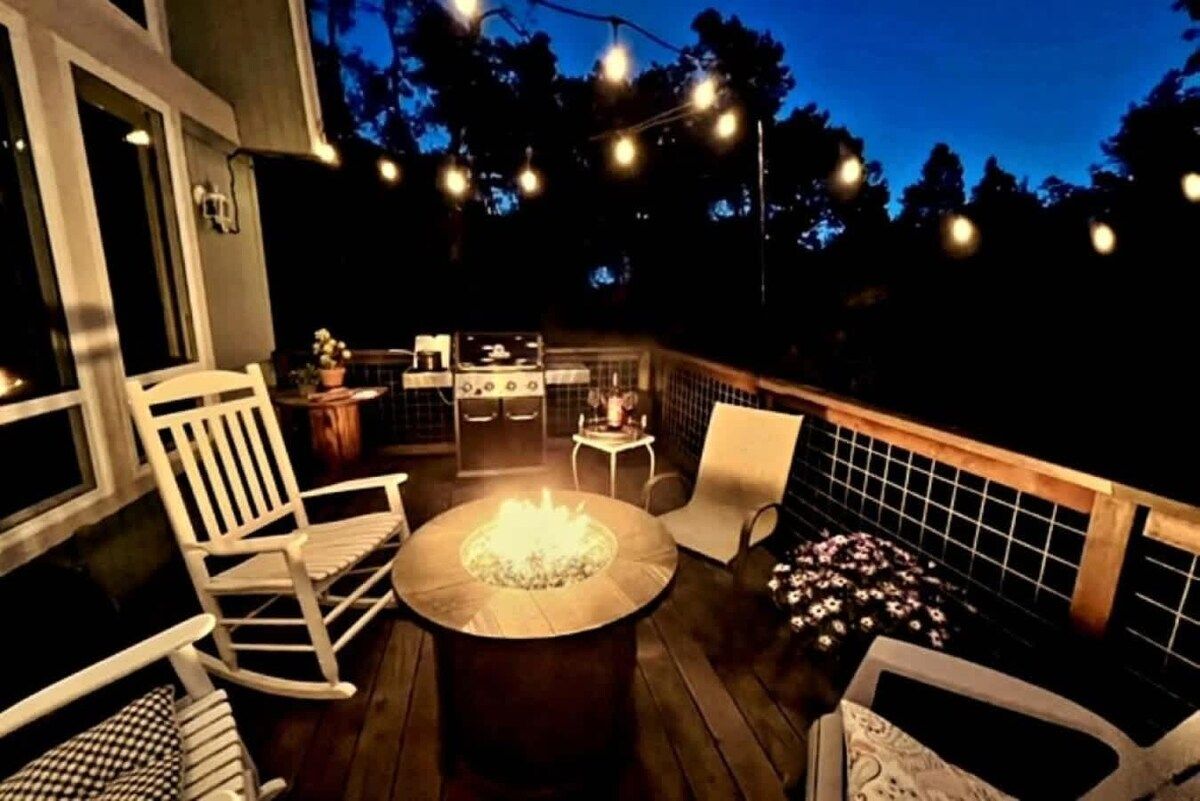 Una terraza exterior con un brasero, asientos e iluminación de luces colgantes.