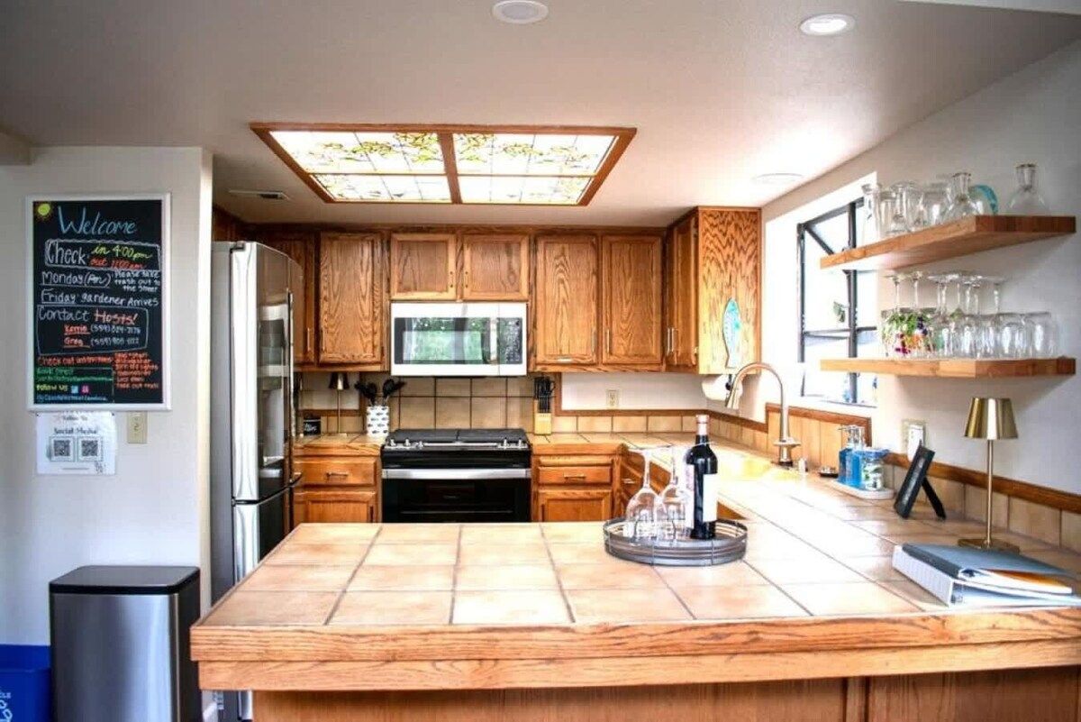 A modern kitchen with wooden cabinets, a central island, and a chalkboard menu on the wall.