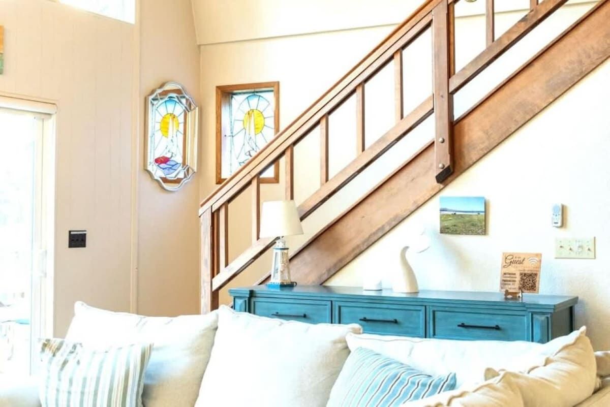 A staircase with wooden railings leading to a landing, a blue dresser with drawers, and two wall-mounted stained glass windows.