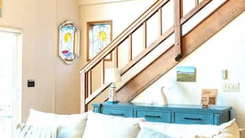 A staircase with wooden railings leading to a landing, a blue dresser with drawers, and two wall-mounted stained glass windows.
