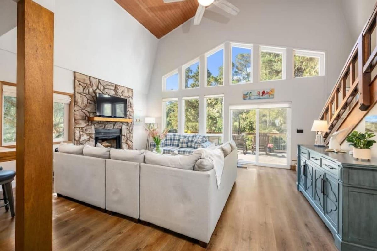A spacious living area with a large sectional sofa, a fireplace, and a view of the outdoors through multiple windows.