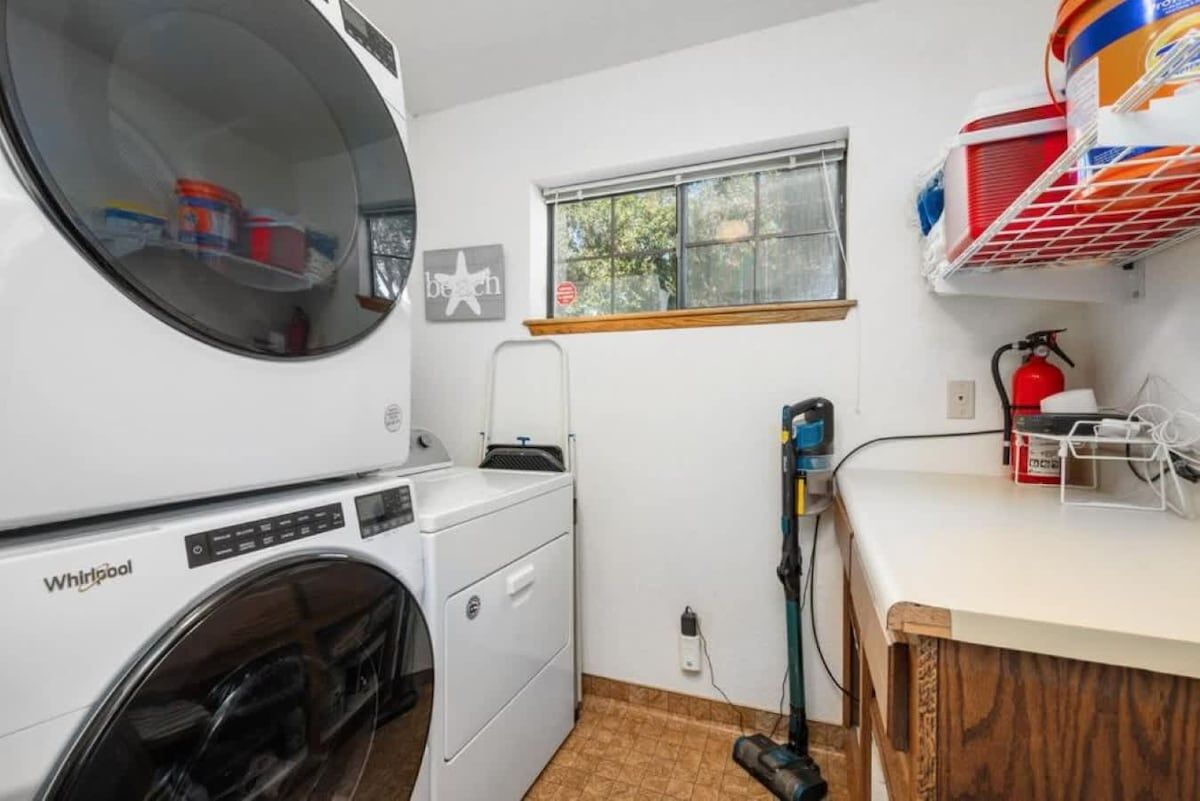 A laundry area with a Whirlpool washer and dryer, a window, a fire extinguisher, and a shelf with cleaning supplies.