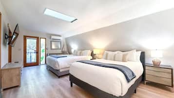 A bedroom with two beds, a skylight, a sliding door to a balcony, and a bedside table with a lamp.