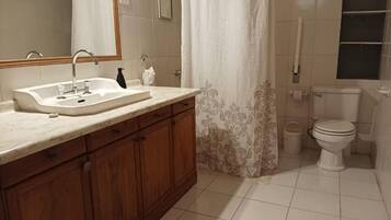 A bathroom with a sink, mirror, wooden cabinets, a toilet, and a shower curtain.