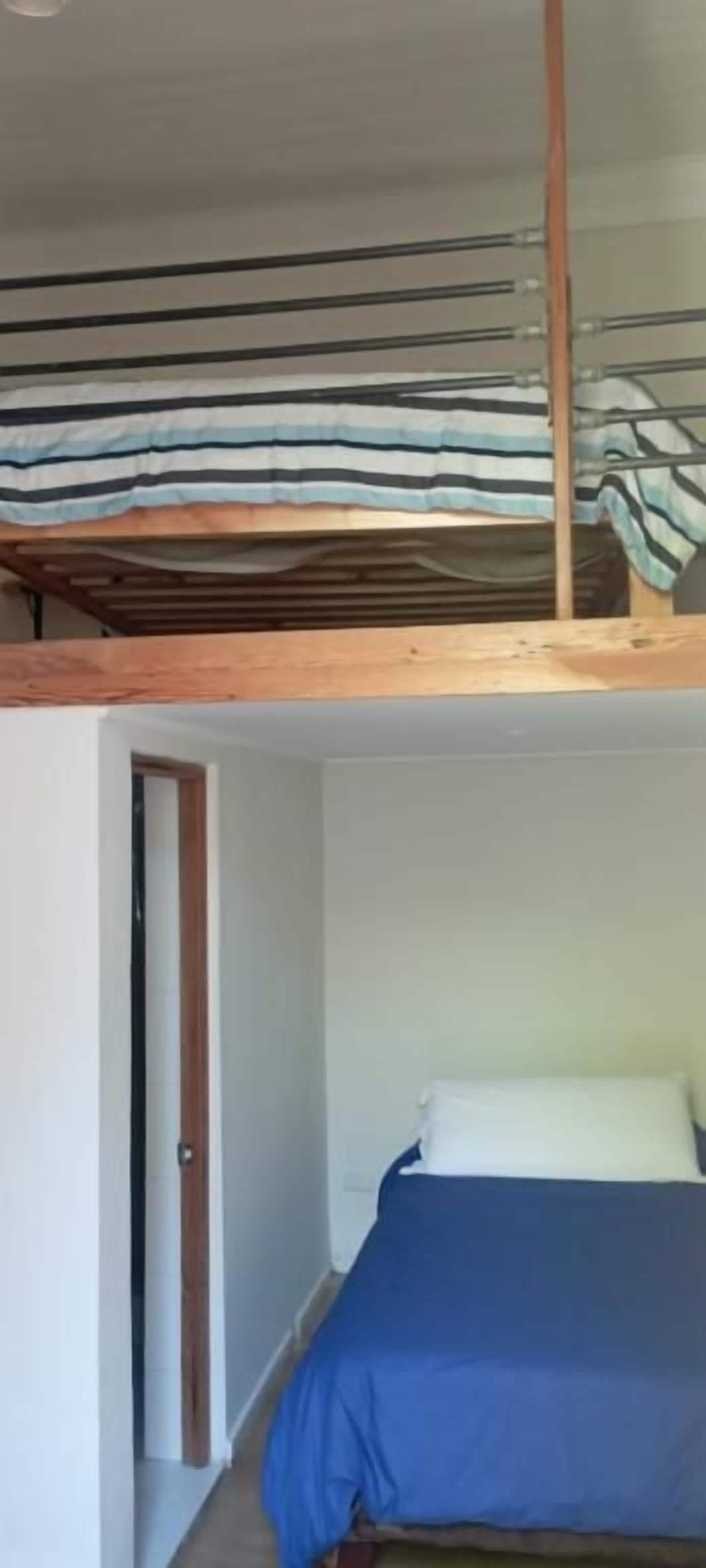 Une chambre avec un lit superposé, une porte et un lit simple recouvert d’une couverture bleue.